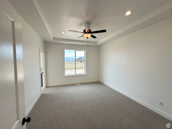Carpeted empty room featuring a textured ceiling, a raised ceiling, ceiling fan, and recessed lighting | Image 13