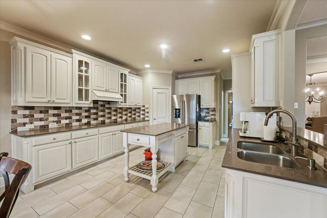 Kitchen with stainless steel fridge with ice dispenser, dark countertops, a sink, under cabinet range hood, and crown molding | Image 14