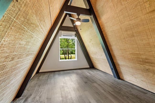 This photo showcases a cozy A-frame room with wood-paneled walls, a ceiling fan, and a large window offering scenic views of greenery. Ideal for a tranquil retreat. | Image 22