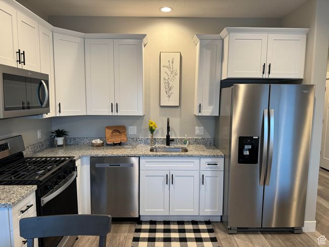 Kitchen with appliances with stainless steel finishes, sink, white cabinetry, light stone counters, and light wood-type flooring | Image 18