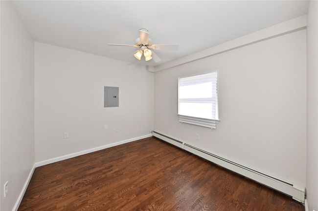 Empty room with electric panel, ceiling fan, dark wood-type flooring, baseboards, and baseboard heating | Image 11
