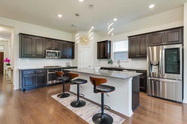 Kitchen featuring appliances with stainless steel finishes, a center island, dark brown cabinetry, decorative backsplash, and a sink | Image 9