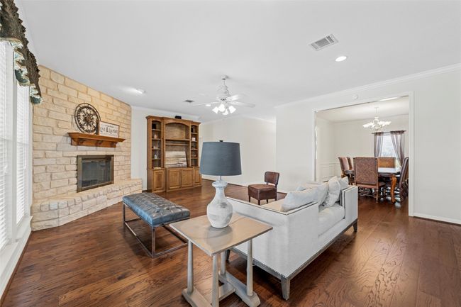 Living room with a fireplace, wood finished floors, visible vents, and crown molding | Image 7