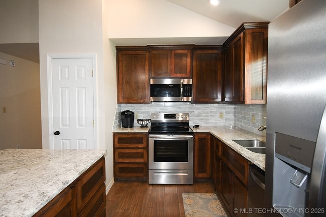 Kitchen featuring appliances with stainless steel finishes, a sink, dark wood-type flooring, vaulted ceiling, and tasteful backsplash | Image 16