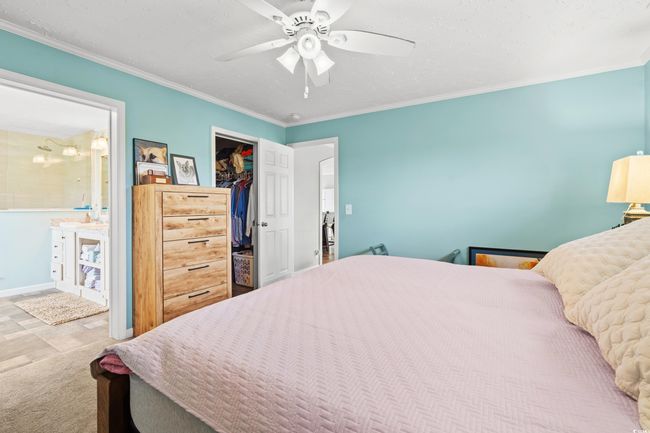 Carpeted bedroom featuring a walk in closet, crown molding, a closet, ceiling fan, and connected bathroom | Image 13