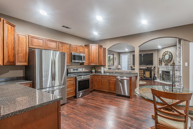 Kitchen featuring appliances with stainless steel finishes, arched walkways, brown cabinetry, dark wood-style flooring, and recessed lighting | Image 4