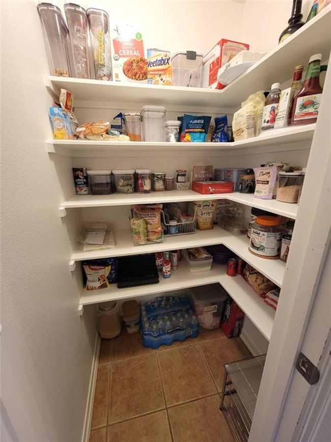 This photo shows a well-organized pantry with several white shelves stocked with various food items and kitchen supplies. The space is bright and neatly arranged, offering ample storage for household essentials. | Image 29
