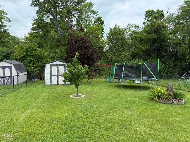 fenced backyard with a storage unit, a playground, and a trampoline | Image 7