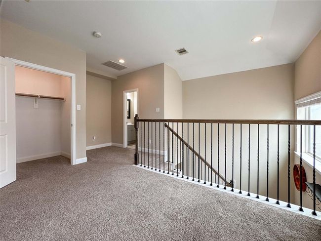 This photo shows a carpeted upstairs landing area with neutral walls and recessed lighting. It features an open railing overlooking the staircase, a window for natural light, and a walk-in closet. There's also an entrance to what appears to be a bathroom. | Image 31