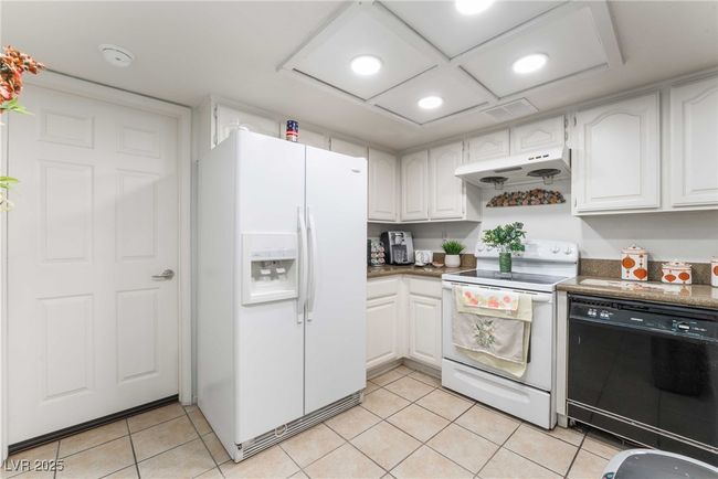 Kitchen with light tile patterned floors, white cabinetry, under cabinet range hood, and white appliances | Image 15
