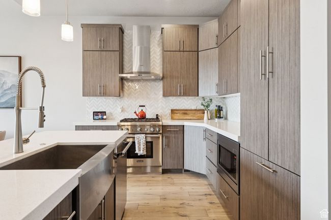 Kitchen featuring wall chimney range hood, stainless steel appliances, light countertops, light wood-style floors, and backsplash | Image 20