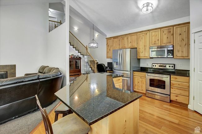 Kitchen featuring dark stone counters, open floor plan, a breakfast bar area, stainless steel appliances, and light wood-style flooring | Image 4