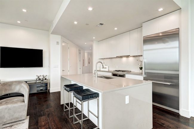 Kitchen featuring built in refrigerator, white cabinetry, dark wood-style floors, a center island with sink, and recessed lighting | Image 10