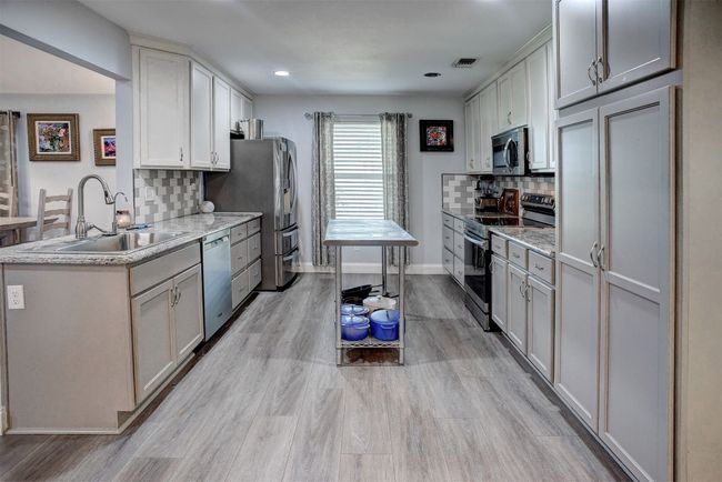 Kitchen featuring stainless steel appliances, tasteful backsplash, light vinyl finished floors, recessed lighting, and light stone counters | Image 12