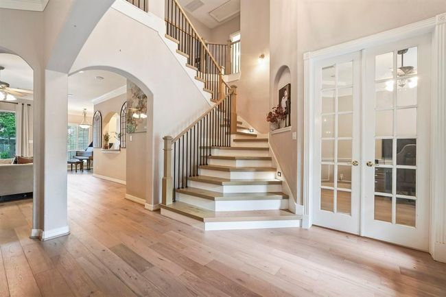 Open entryway with elegant wood flooring and a striking staircase. Arched doorways and French doors to office adds charm. | Image 4