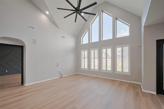 This spacious room features high vaulted ceilings, a modern ceiling fan, and large floor-to-ceiling windows with shutters, allowing ample natural light. | Image 4