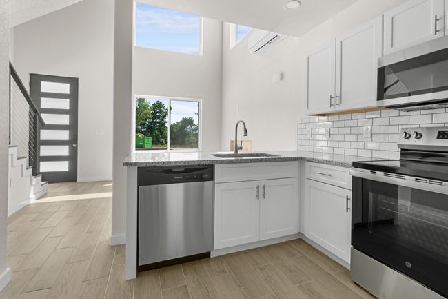 Kitchen with stainless steel appliances, light stone counters, white cabinets, a wall unit AC, and a high ceiling | Image 8