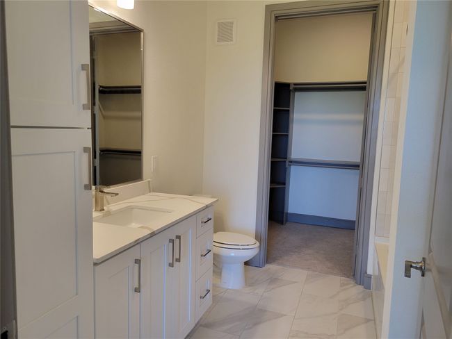 Bathroom with toilet, marble look tile flooring, a walk in closet, and vanity | Image 12