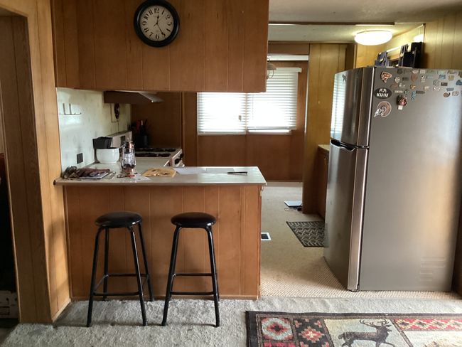 Kitchen featuring freestanding refrigerator, light colored carpet, a peninsula, brown cabinets, and under cabinet range hood | Image 4