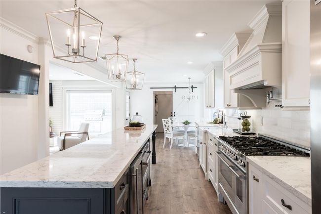 This kitchen features an 8 burner gas range, large farmhouse sink, marble backsplash, beverage fridge, and ice maker. | Image 10
