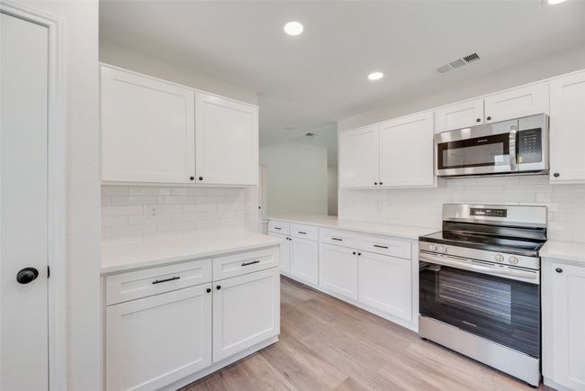 Kitchen with appliances with stainless steel finishes, light countertops, white cabinetry, recessed lighting, and light wood-style flooring | Image 10