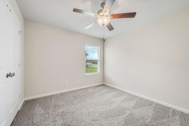 Spacious secondary bedroom with ceiling fan, large window, and plush carpeting. | Image 12