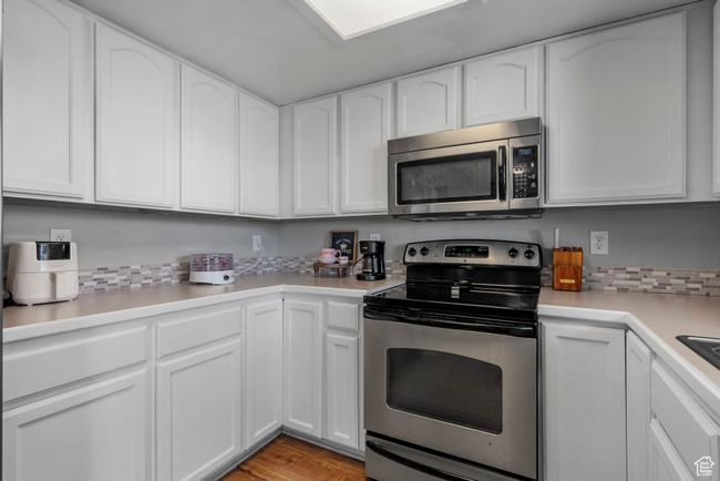 Kitchen with appliances with stainless steel finishes, white cabinets, light countertops, light wood-style flooring, and tasteful backsplash | Image 10