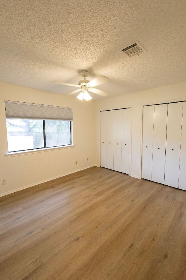 Unfurnished bedroom featuring two closets, a textured ceiling, wood finished floors, baseboards, and a ceiling fan | Image 18