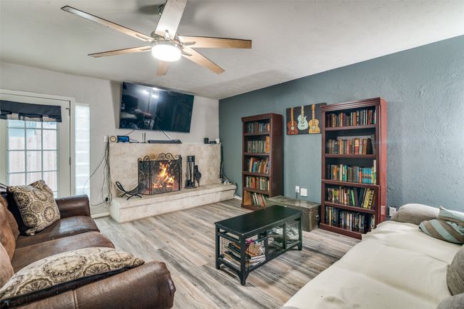 Living area with a textured wall, wood finished floors, a lit fireplace, and ceiling fan | Image 9