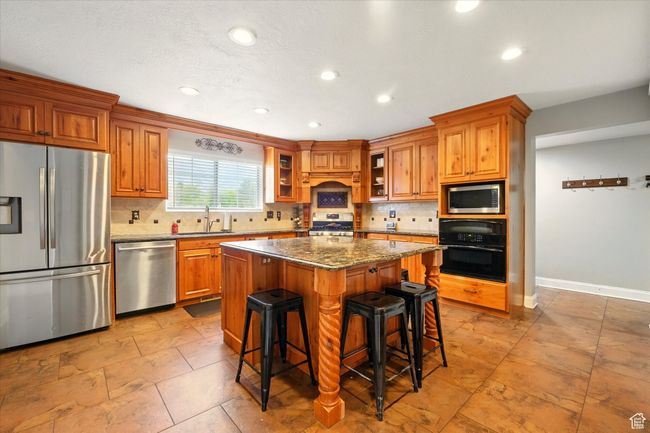 Kitchen featuring stainless steel appliances, brown cabinets, tasteful backsplash, recessed lighting, and a kitchen island | Image 24