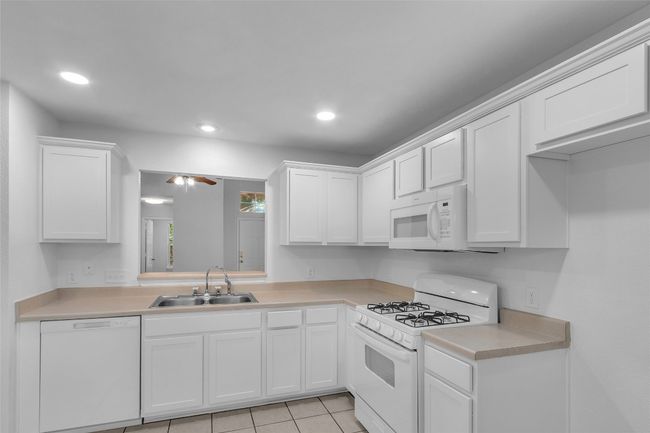 Kitchen with white appliances, light countertops, white cabinetry, light tile patterned floors, and recessed lighting | Image 13