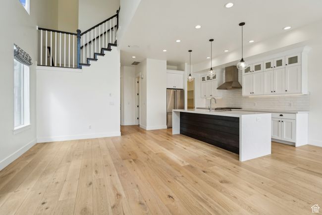 Kitchen with light wood-type flooring, a sink, wall chimney range hood, light countertops, and high end refrigerator | Image 19