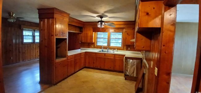Kitchen with ceiling fan, brown cabinetry, wooden walls, and plenty of natural light | Image 17