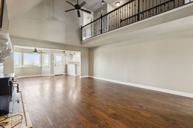 Unfurnished living room with a ceiling fan, wood finished floors, baseboards, and a towering ceiling | Image 10