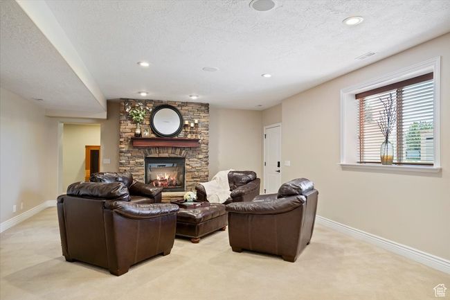 Living room with baseboards, a textured ceiling, a stone fireplace, and light colored carpet | Image 21