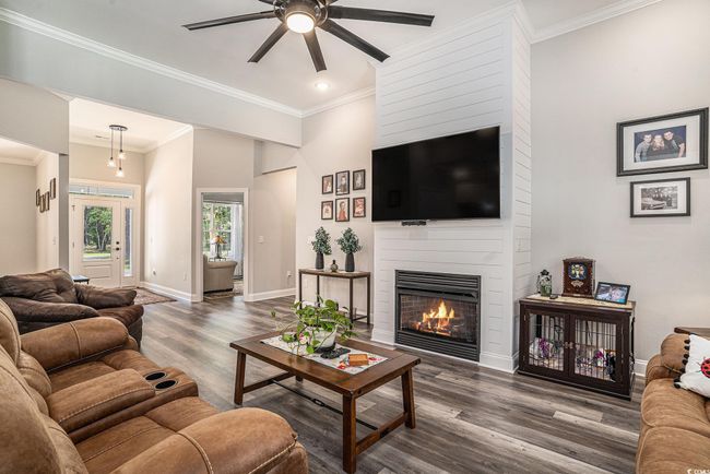 Living room featuring a large fireplace, a ceiling fan, wood finished floors, baseboards, and crown molding | Image 17
