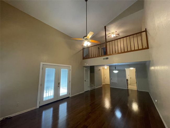 Unfurnished living room featuring high vaulted ceiling, baseboards, wood finished floors, french doors, and ceiling fan | Image 24