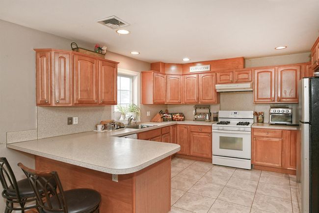 Kitchen featuring a sink, freestanding refrigerator, white range with gas cooktop, a peninsula, and under cabinet range hood | Image 15
