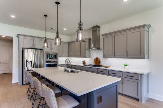 Kitchen featuring appliances with stainless steel finishes, gray cabinetry, wall chimney range hood, light wood finished floors, and recessed lighting | Image 18