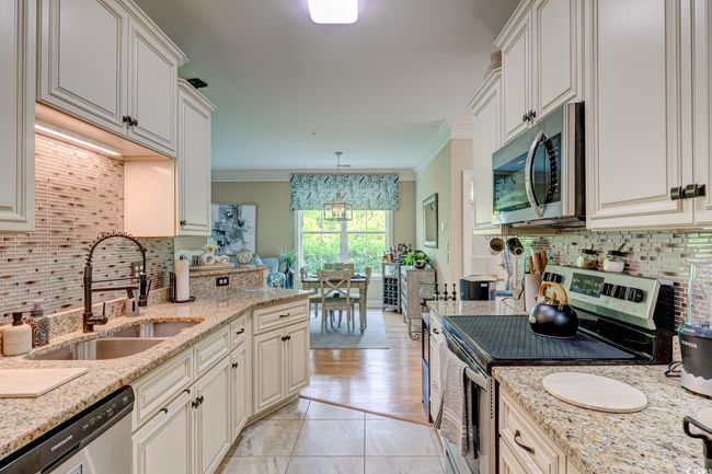 Kitchen with stainless steel appliances, a sink, decorative backsplash, crown molding, and light stone countertops | Image 8