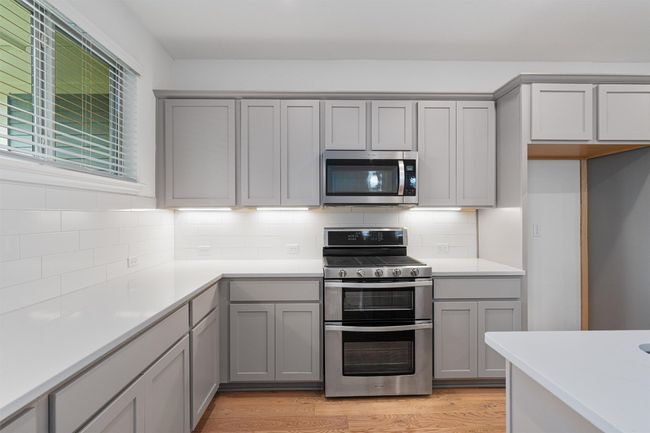 Kitchen featuring stainless steel appliances, light wood flooring, tasteful backsplash, light gray cabinetry, & quartz countertops. Gas range, two ovens | Image 7