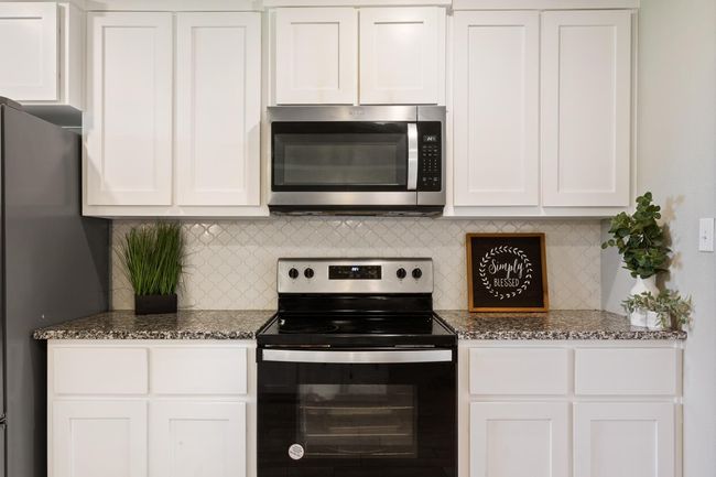 Kitchen featuring stainless steel appliances, white cabinets, dark stone counters, and decorative backsplash | Image 14
