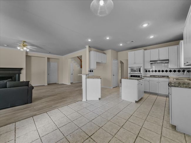 Kitchen featuring open floor plan, decorative backsplash, white cabinets, light tile patterned flooring, and ceiling fan | Image 7