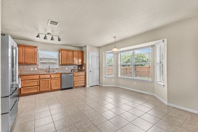 Kitchen featuring appliances with stainless steel finishes, light tile patterned flooring, decorative backsplash, a textured ceiling, and light countertops | Image 19