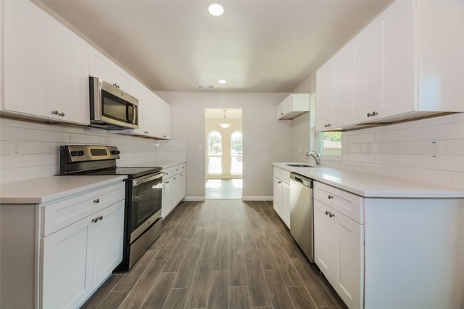 Kitchen featuring appliances with stainless steel finishes, recessed lighting, decorative backsplash, white cabinetry, and light countertops | Image 12