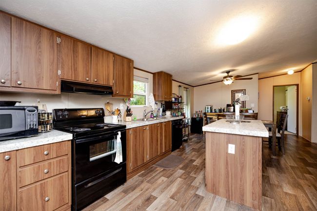 Kitchen featuring under cabinet range hood, brown cabinets, black appliances, and ceiling fan | Image 7