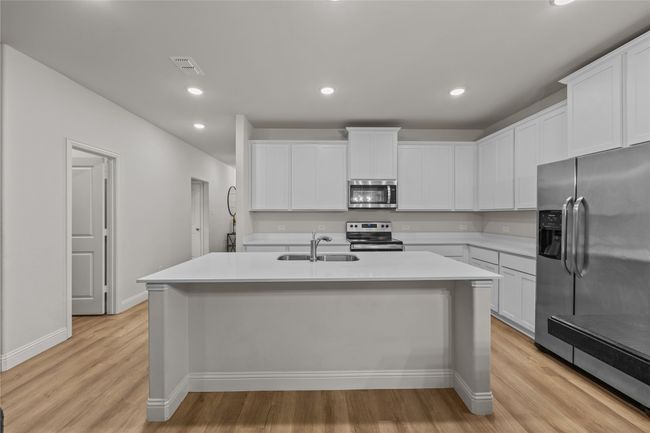 Kitchen featuring appliances with stainless steel finishes, a sink, light countertops, a center island with sink, and light wood-type flooring | Image 14
