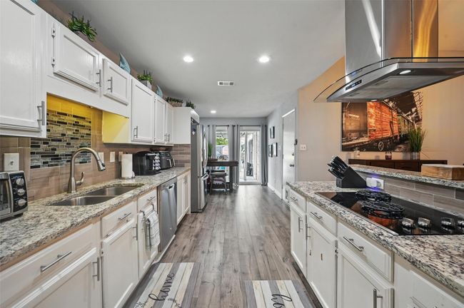 Kitchen featuring island exhaust hood, appliances with stainless steel finishes, decorative backsplash, white cabinetry, and recessed lighting | Image 14