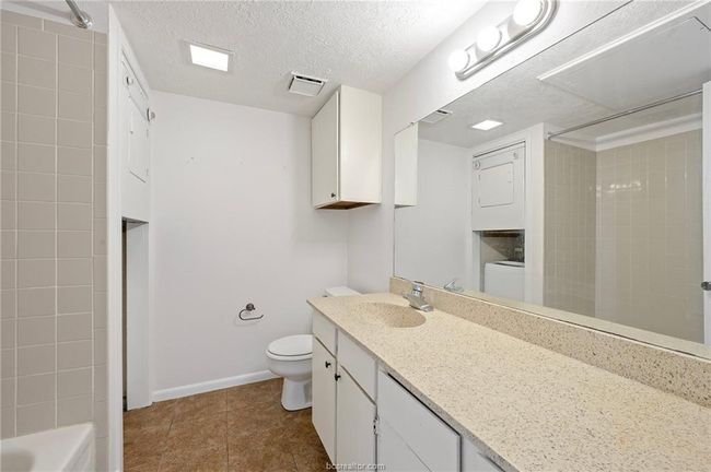 Full bath with vanity, a textured ceiling, dark tile patterned flooring, shower / bath combination, and stacked washer / drying machine | Image 10