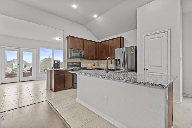 Kitchen featuring black appliances, a sink, vaulted ceiling, light stone countertops, and tasteful backsplash | Image 9